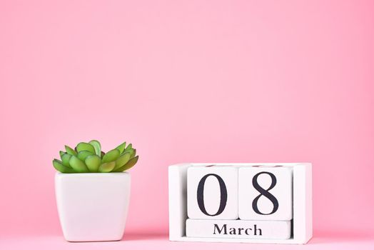 Women's Day concept. Wooden calendar block with date 8 march and plant on pink background with copy space