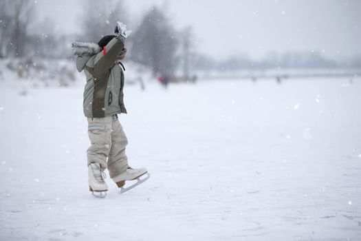 The child learn to skate a huge size on the lake. A boy ice skating on an ice river on a snowy winter day