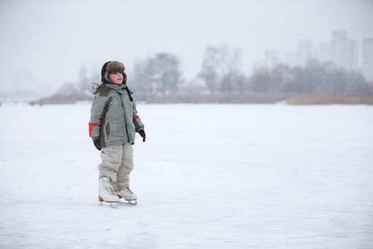 A little boy in huge skates is riding on the lake.Entertainment on a winter day for a child.