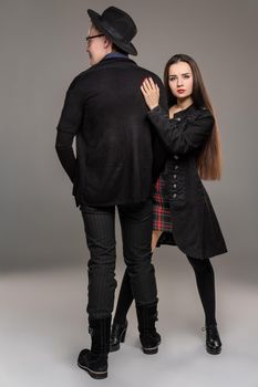 Young loving couple. Studio shot of a charming young female and male. They are in black outlet clothes and stylish hat posing over a gray studio background. Fashion shot. Sincere emotions concept. Copy space.