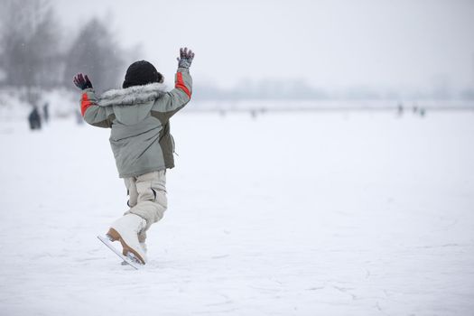 A little boy in huge skates is riding on the lake