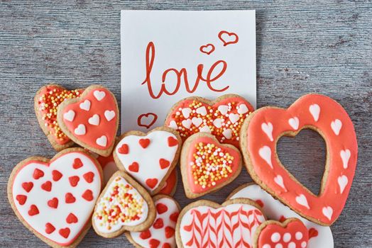 Decorated and glazed heart shape cookies and paper note with inscription LOVE on gray background, top view. Valentines day concept