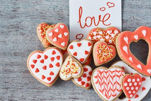 Decorated and glazed heart shape cookies and paper note with inscription LOVE on gray background, top view. Valentines day concept