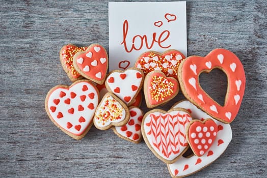 Decorated and glazed heart shape cookies and paper note with inscription LOVE on gray background, top view. Valentines day concept