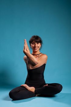 Portrait of smiling zen woman trainer standing in lotus position holding arms in crossed position practicing spiritual meditation. Athletic person working at healthy lifestyle stretching body muscles