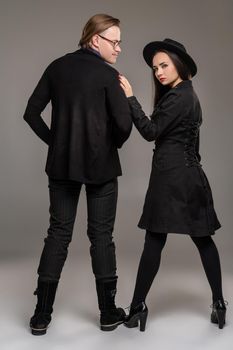 Young loving couple. Studio shot of a beautiful young woman and man. They are in black outlet clothes and stylish hat posing over a gray studio background. Fashion shot. Sincere emotions concept. Copy space.