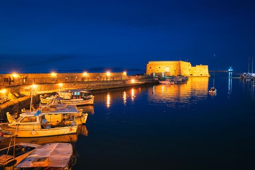 Venetian Fort castle in Heraklion and moored Greek fishing boats in port, Crete Island, Greece in the evening