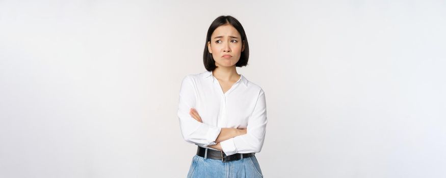 Image of sad office girl, asian woman sulking and frowning disappointed, standing upset and distressed against white background.