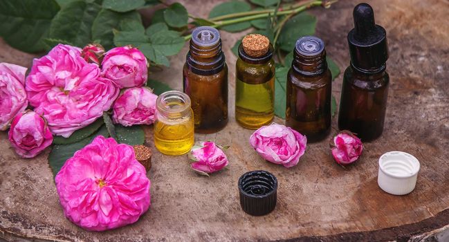 Close-up of rose essential oil bottle with falling leaves on wooden background. Selective focus