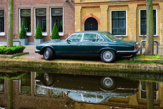 Old black retro car on canal embankment in street of Delft with reflection. Delft, Netherlands