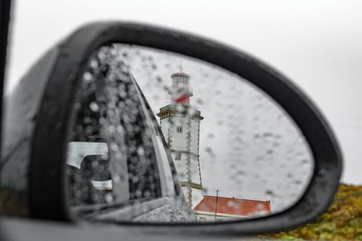 Rain over car rear-view mirror with Lighthouse
