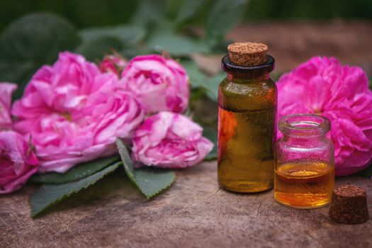 Close-up of rose essential oil bottle with falling leaves on wooden background. Selective focus