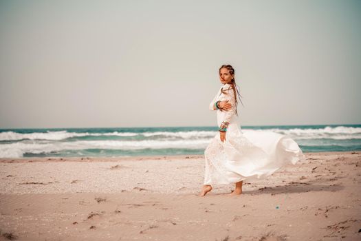 Model in boho style in a white long dress and silver jewelry on the beach. Her hair is braided, and there are many bracelets on her arms