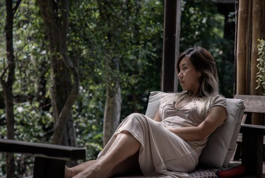 Young woman enjoys the nature while sits on cozy wooden balcony of a wooden country house. Concept of solitude and recreation on nature. Selective focus.