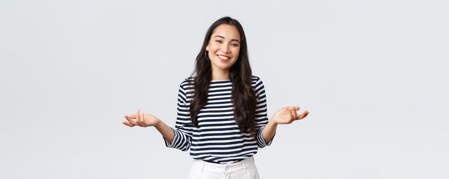 Lifestyle, beauty and fashion, people emotions concept. Smiling cute clueless girl dont have idea, no answer, shrugging with hands spread sideways, standing white background.