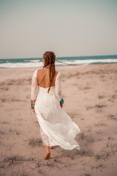 Model in boho style in a white long dress and silver jewelry on the beach. Her hair is braided, and there are many bracelets on her arms