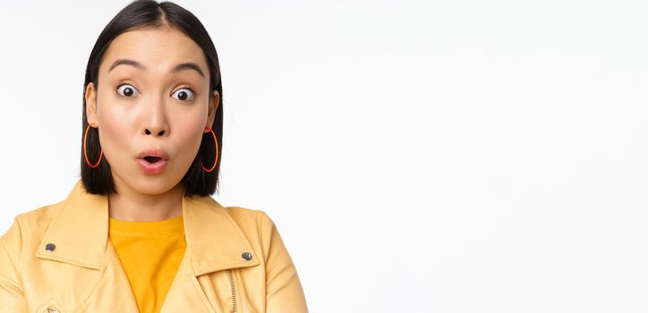 Close up of impressed asian girl, say wow, looking amazed at camera, standing in casual clothes over white background. Copy space