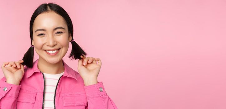 Skin care and cosmetology concept. Beautiful asian girl smiling and laughing, showing clean healthy facial skin, posing against pink background. Copy space
