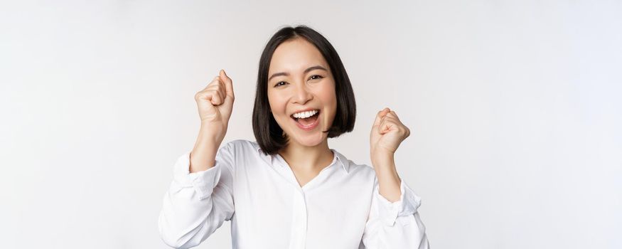 Close up face portrait of dancing asian woman smiling, triumphing and celebrating with happy emotion, standing over white background. Copy space