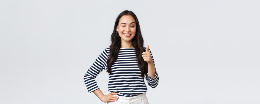 Lifestyle, beauty and fashion, people emotions concept. Cheerful cute asian girl thumb-up in approval, wink encouraging and smiling, praising nice job, say well played as congratulate with win.