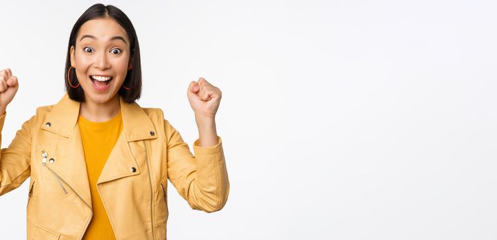 Image of asian woman dancing and smiling happy, celebrating victory, triumphing, standing over white background. copy space