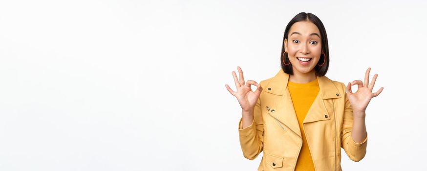 Beautiful korean girl with happy face, looking satisfied, showing okay, ok gesture, recommending shop, like and approve smth good, excellent quality, white background.