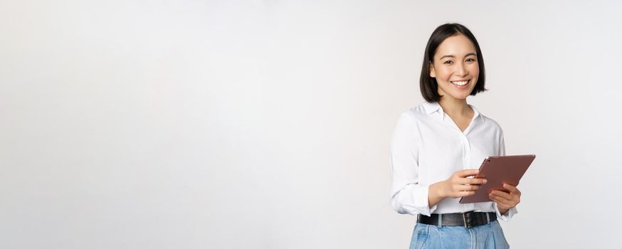 Image of young ceo manager, korean working woman holding tablet and smiling, standing over white background.