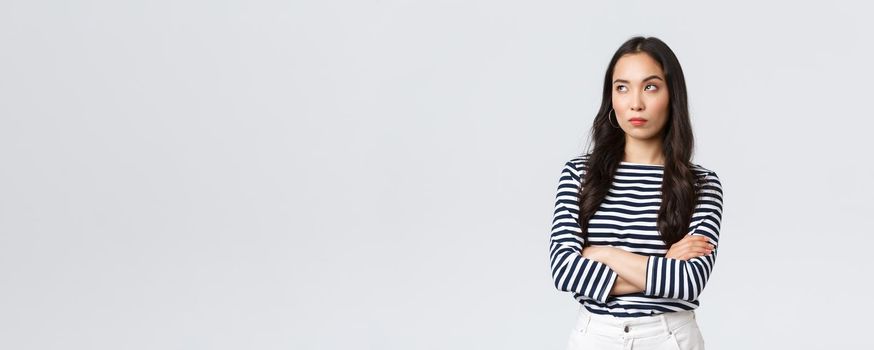 Lifestyle, beauty and fashion, people emotions concept. Annoyed and uninterested asian woman roll eyes, looking away bothered and bored, cross arms chest, standing white background.