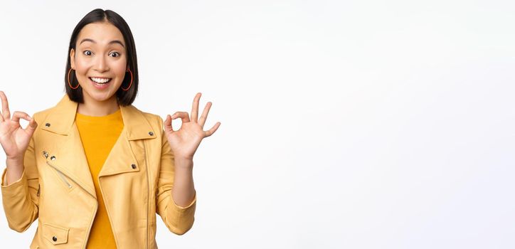 Beautiful korean girl with happy face, looking satisfied, showing okay, ok gesture, recommending shop, like and approve smth good, excellent quality, white background.