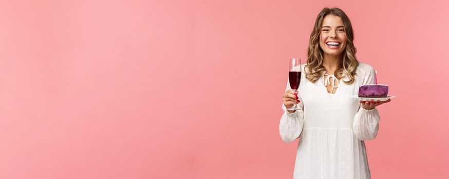 Holidays, spring and party concept. Portrait of excited good-looking young tender girl celebrating birthday, having fun with friends, eating b-day cake and drink wine from glass, laughing joyfully.