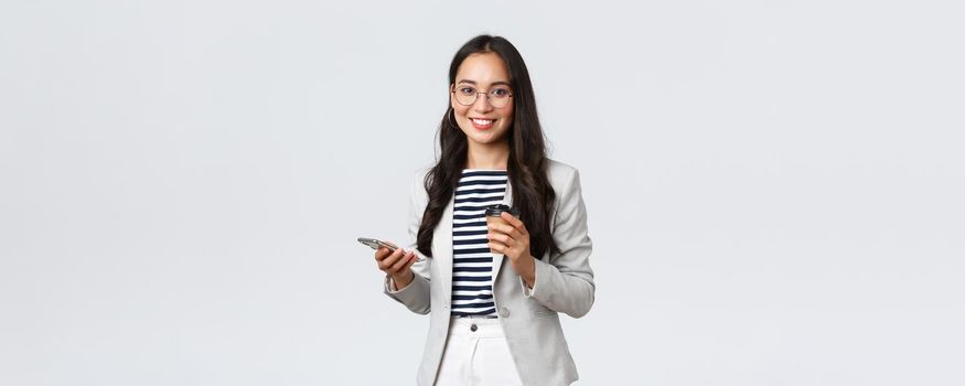 Business, finance and employment, female successful entrepreneurs concept. Professional asian businesswoman in glasses, having lunch, drinking takeaway coffee and using mobile phone.