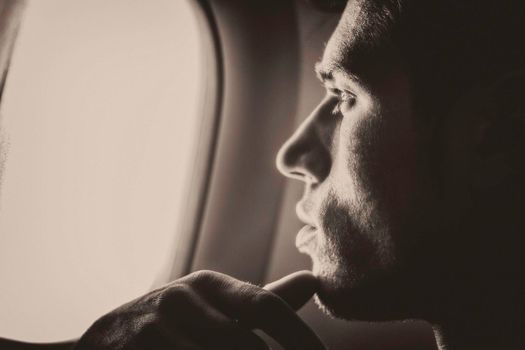 Side view of handsome young man against plane window sitting