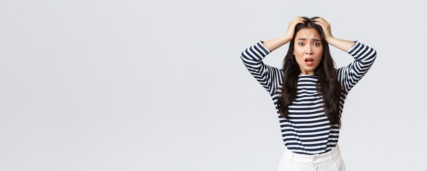 Lifestyle, people emotions and casual concept. Troubled young woman stare alarmed, feel bad as something awful happened, grab head and stare camera anxious, white background.