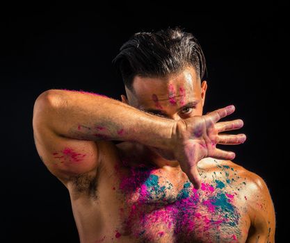 Muscular young man shirtless with skin painted with Holi colors, looking at camera