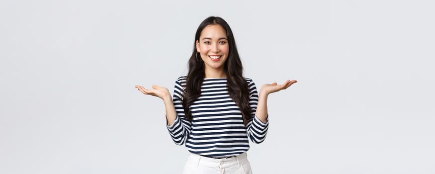 Lifestyle, people emotions and casual concept. Cute smiling asian woman introduce two products, hold hands sideways as if demonstrating products on palms, standing white background.