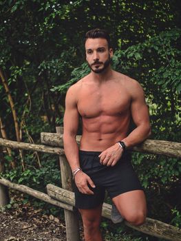 Handsome Muscular Shirtless Hunk Man Outdoor in Country Leaning Against Wood Fence. Showing Healthy Muscle Body While Looking at Camera