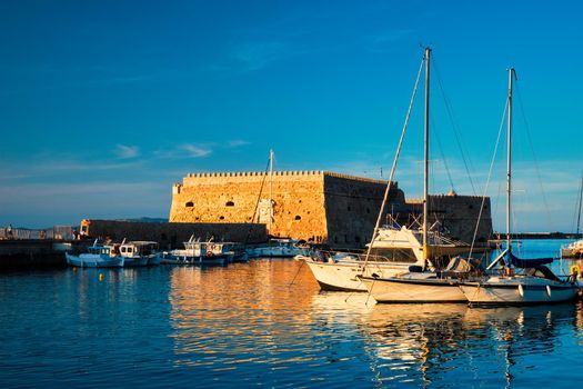 Venetian Fort Venetian fortress of Koules Castello a Mare castle in Heraklion and moored Greek fishing boats in port, Crete Island, Greece on sunset