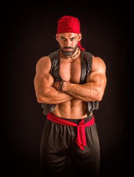 Muscular male pirate in studio shot, wearing bandana and open leather vest on naked muscle torso, looking at camera