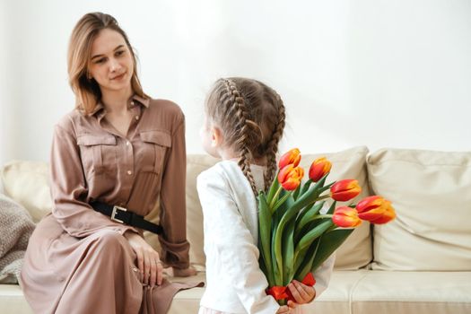 Happy daughter congratulates mom with tulips at home in the living room