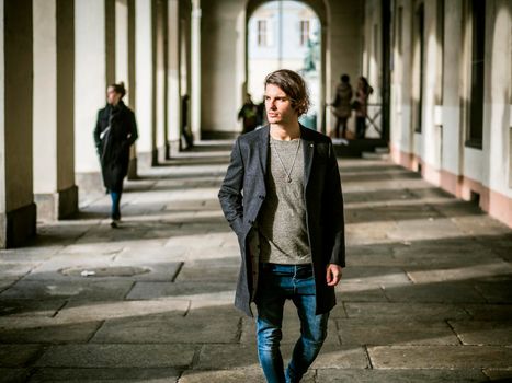 Elegant attractive young man outdoor wearing wool coat, in European city under colonnade in city center