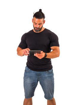 Attractive muscular man using electronic tablet, tapping on it, standing in studio shot isolated on white