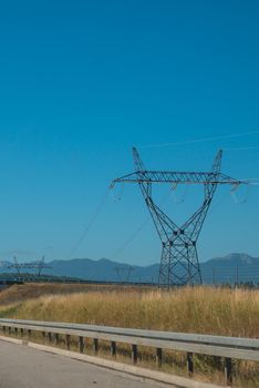 High voltage pole with blue sky, blue sky, trees and grass.