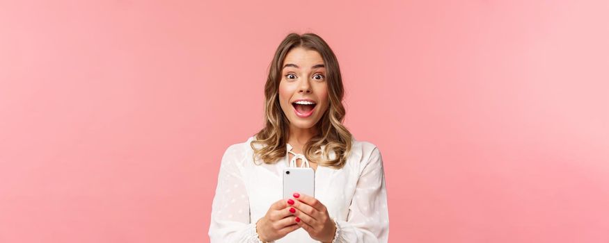 Close-up portrait of excited and amazed young blond girl attend performance of favorite singer, record video, stream online on mobile phone, taking photo with smartphone, look thrilled.