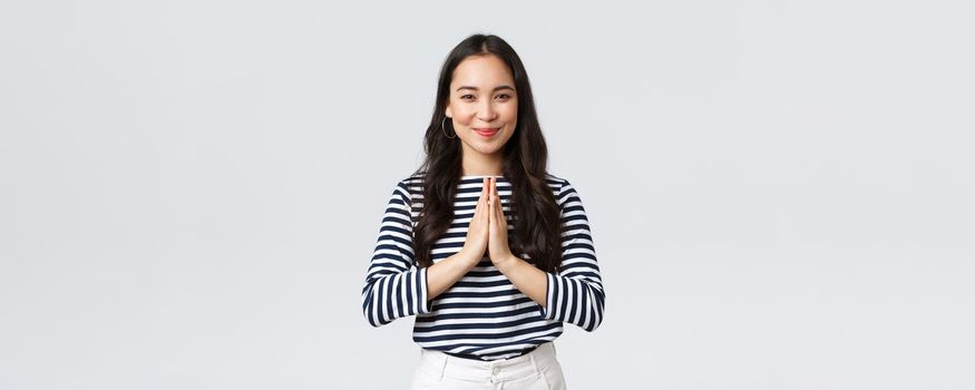 Lifestyle, people emotions and casual concept. Cute asian girl in casual outfit smiling as saying namaste, holding hands in pray, pleading or greeting guests with polite bow.