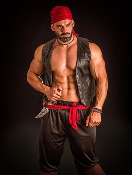 Muscular male pirate in studio shot, wearing bandana and open leather vest on naked muscle torso