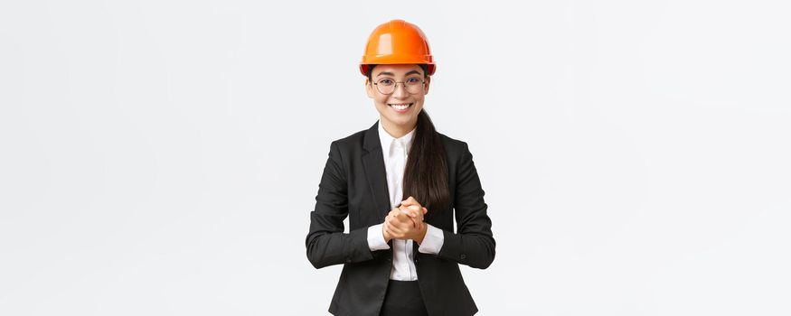 Smiling professional asian businesswoman in safety helmet and business suit introducing enterprise to clients or investors, showing around, making presentation at construction area.