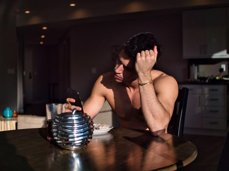 Young shirtless man using cell phone at table in the morning during breakfast