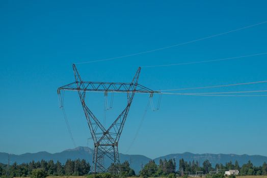 High voltage pole with blue sky, blue sky, trees and grass.