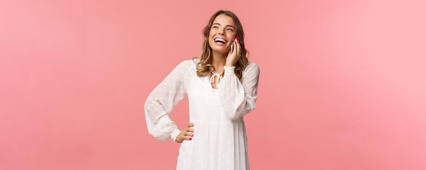 Portrait of carefree good-looking girl with blond short hair, wear white dress, laughing happy as talking on phone, hear funny joke, have conversation using mobile, hold smartphone and chuckle.