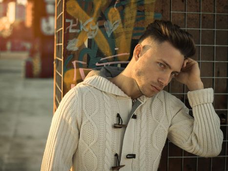 Handsome young man in city setting, with industrial site around him, looking away, serious expression